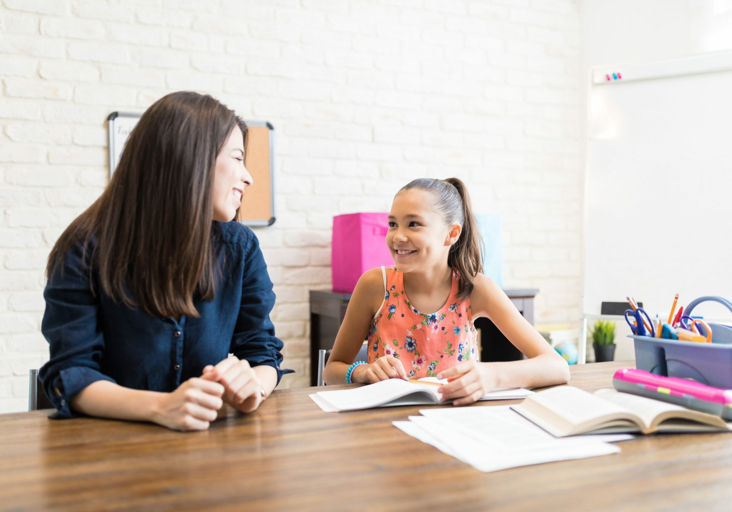 Private Tutor And Student Looking At Each Other At Table Private tutor and female student looking at each other during homeschooling at table
